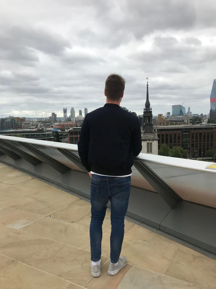 Junger Mann steht auf einer Dachterrasse und blickt über die Skyline einer Großstadt