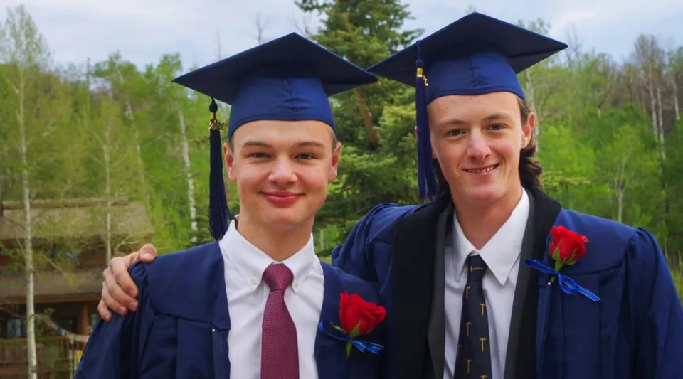 Due studenti della Steamboat Mountain School stanno all'aperto indossando la toga di diploma.