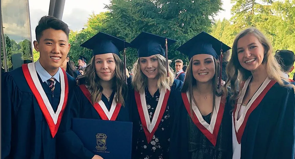 Un gruppo di diplomati della Yale Secondary School sta all'aperto davanti ad alberi e aree verdi.