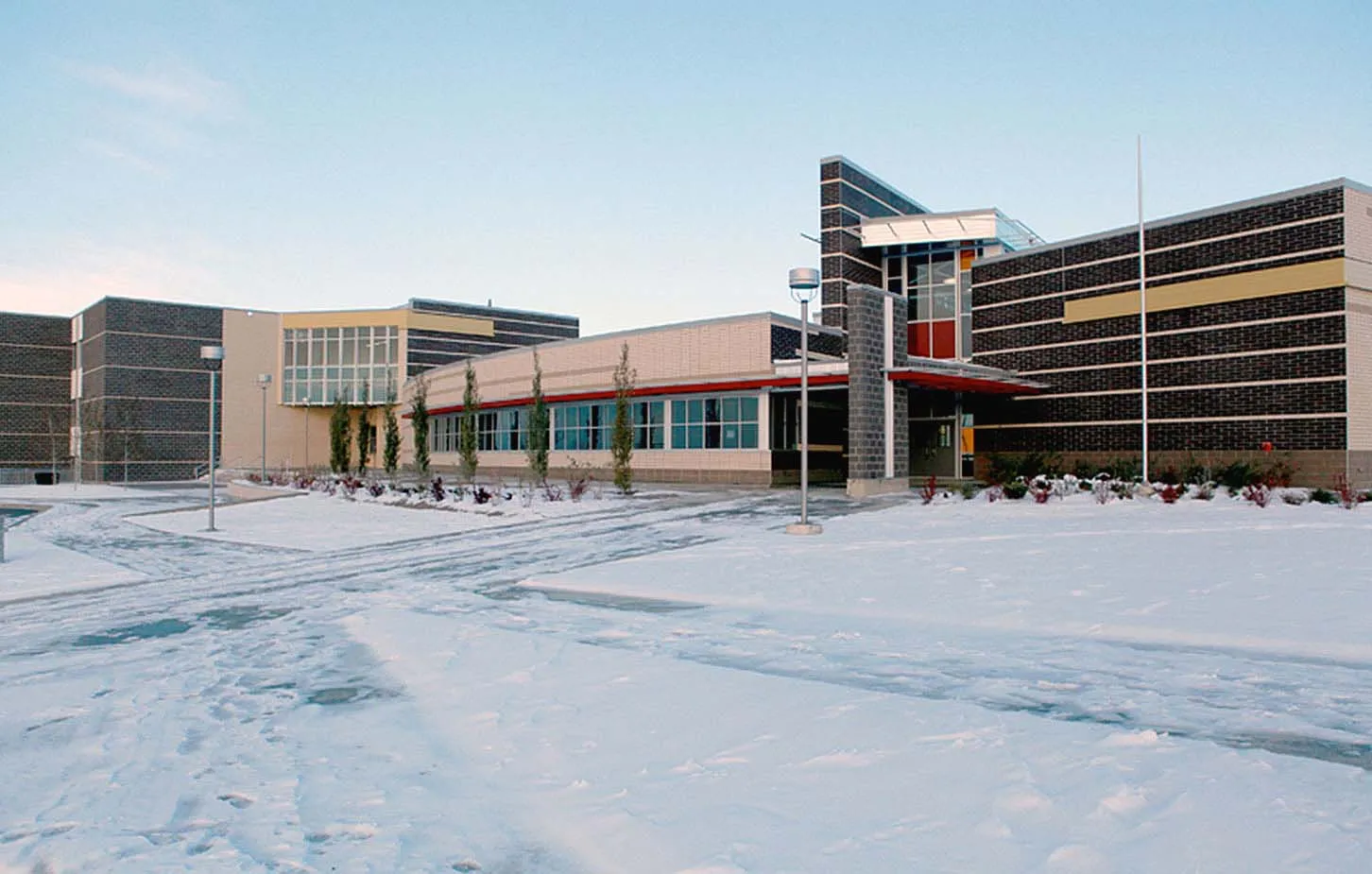 El moderno edificio de varios pisos con fachada de vidrio de la Robert Thirsk High School está rodeado por un paisaje nevado.