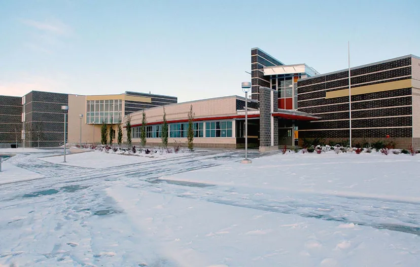 L'edificio moderno a più piani con facciata in vetro della Robert Thirsk High School è circondato da un paesaggio innevato.