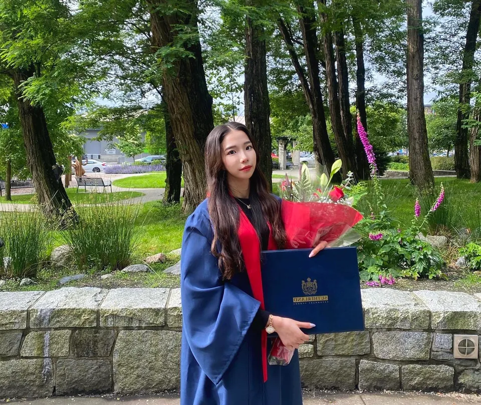 Una studentessa della Sutherland Secondary School si trova nel bosco e tiene in mano un mazzo di fiori e un attestato blu.
