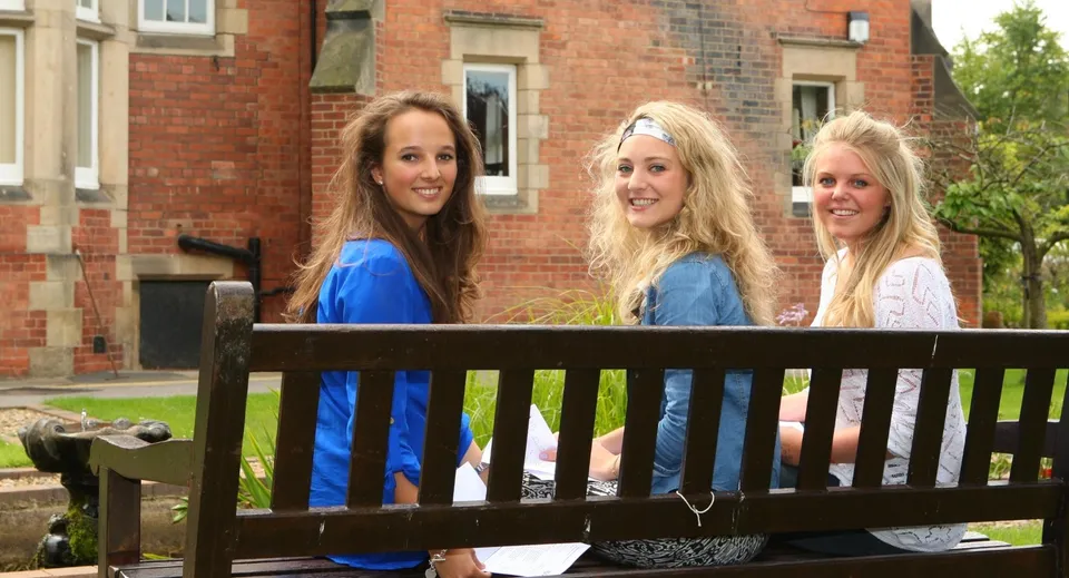 Tre studentesse sono sul balcone davanti a un edificio in mattoni nel campus dell'Harrogate Ladies’ College.