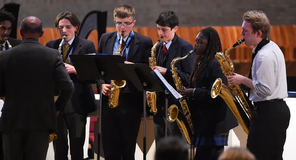 Studenti della Worth School in abito formale si trovano su un palco e si preparano a un'esibizione con i loro strumenti musicali.