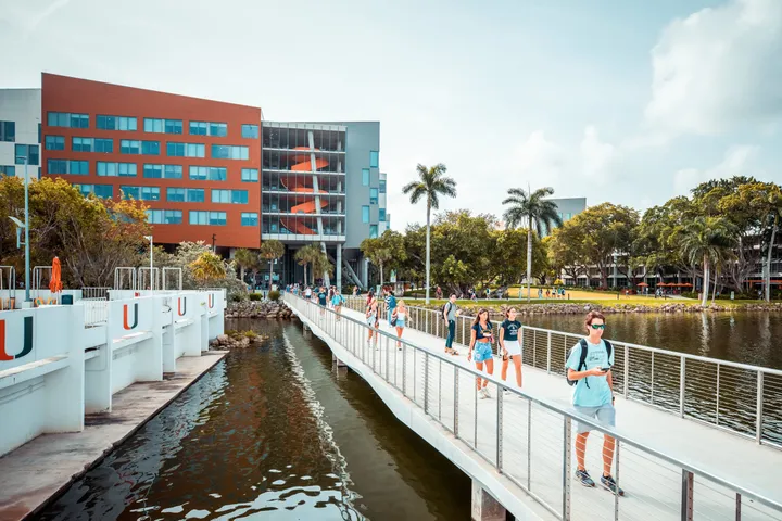 Campus universitario a Miami con studenti sul ponte, edifici moderni, palme e spazi verdi affacciati sull’acqua.