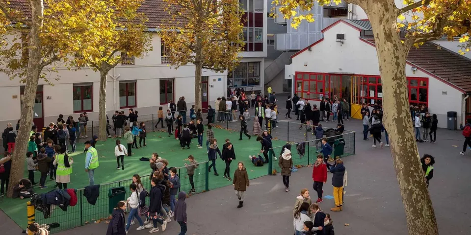 Persone passeggiano su un sentiero coperto da un tappeto verde tra le variopinte foglie autunnali vicino alla École Jeannine Manuel.