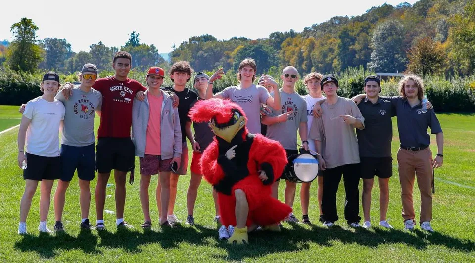 Un gruppo di studenti e studentesse sul campo sportivo della South Kent School, con uno sfondo boschivo.
