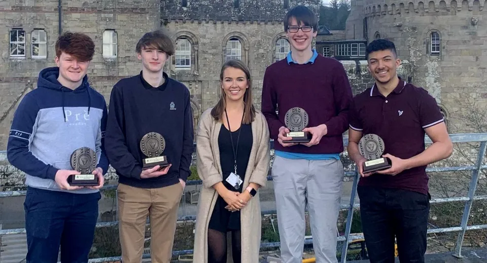 Cinque studenti della Glenstal Abbey School stanno in piedi davanti a uno storico edificio in pietra con dei premi in mano.