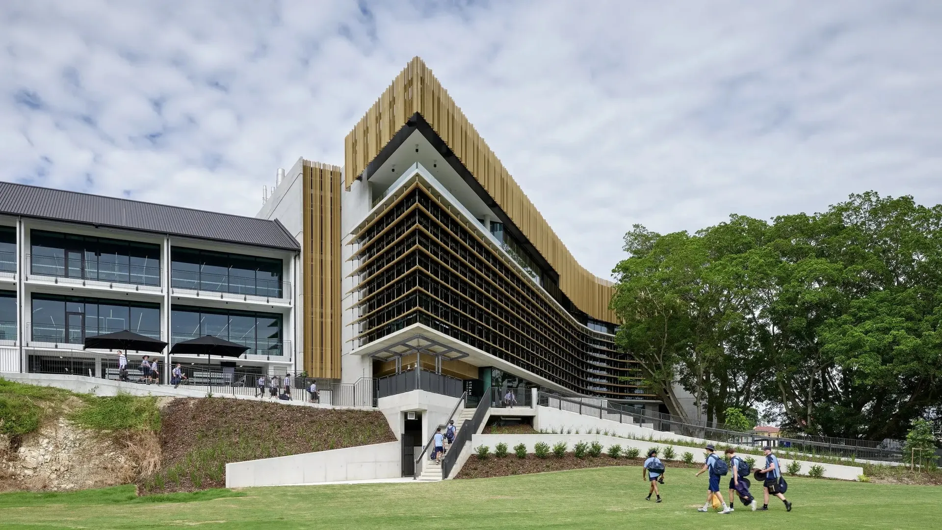 Il moderno edificio della Brisbane Grammar School con una facciata color oro si trova su una collina erbosa sotto un cielo nuvoloso.