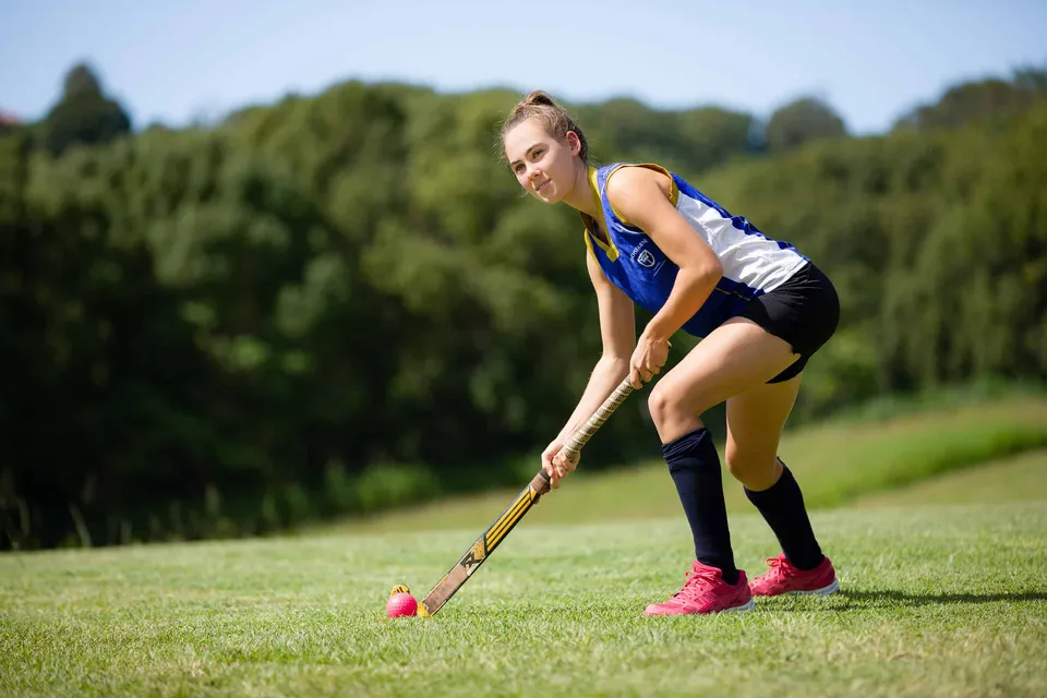 Una studentessa della Lindisfarne Anglican Grammar School gioca a hockey su prato su un campo verde.