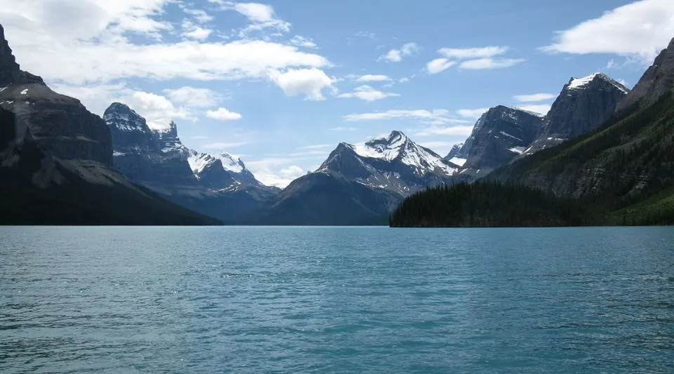 Un tranquillo lago di montagna immerso tra montagne innevate sotto un cielo parzialmente nuvoloso.