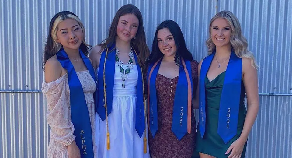 Quattro studentesse della Alpha School sono in piedi in abiti colorati davanti a una parete di lamiera ondulata blu.