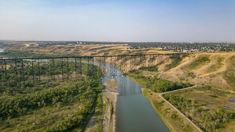 Un lungo ponte ferroviario in acciaio attraversa una valle con fiume nei pressi del Lethbridge Collegiate Institute.