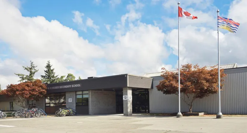 L'edificio moderno di colore nero della R.C. Palmer Secondary School è circondato da alberi e mostra diverse bandiere nazionali all'esterno.