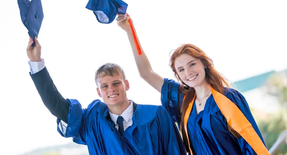 Due diplomati festeggiano all'aperto il loro diploma alla Sotogrande International School indossando toghe blu e arancioni.
