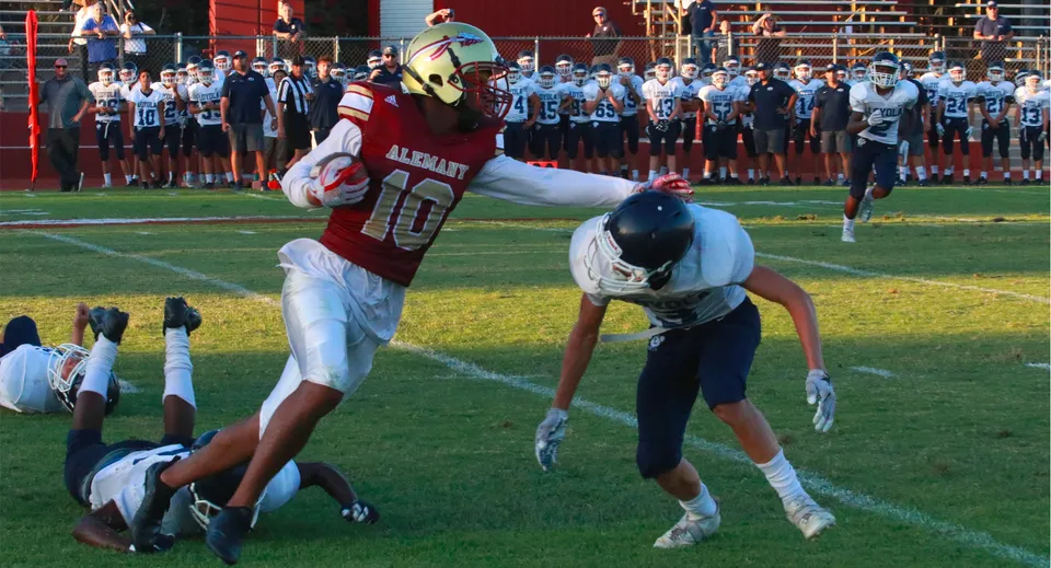 Un giocatore di football della Bishop Alemany High School in maglia rossa esegue un tackle contro un avversario sul campo di gioco.
