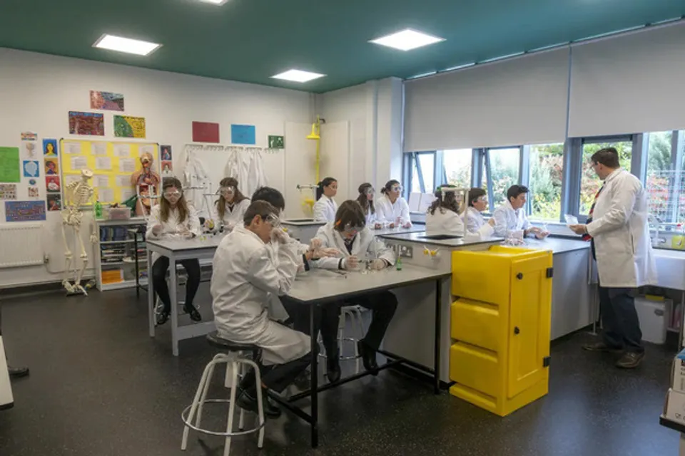 Studenti e un docente della SEK International School Dublin lavorano in camice bianco ai tavoli del laboratorio.