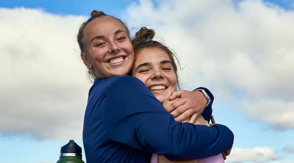 Due persone sorridenti si abbracciano davanti al cielo nuvoloso nel campus della Dublin School.
