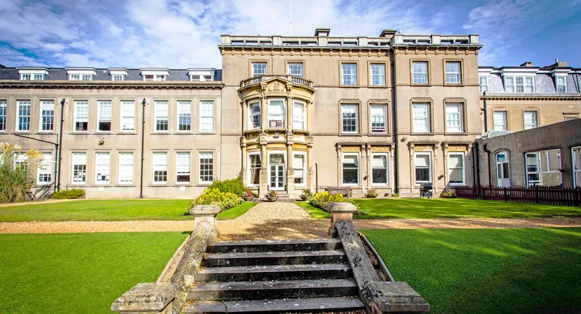 L'edificio principale della Bournemouth Collegiate School con un prato ben curato e scalinate in pietra sotto un cielo blu.