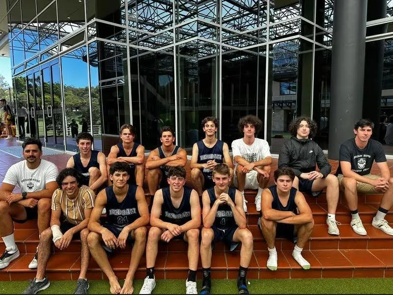 Un grupo de estudiantes de Reddam House con ropa deportiva se sienta en las escaleras frente a un edificio de cristal.