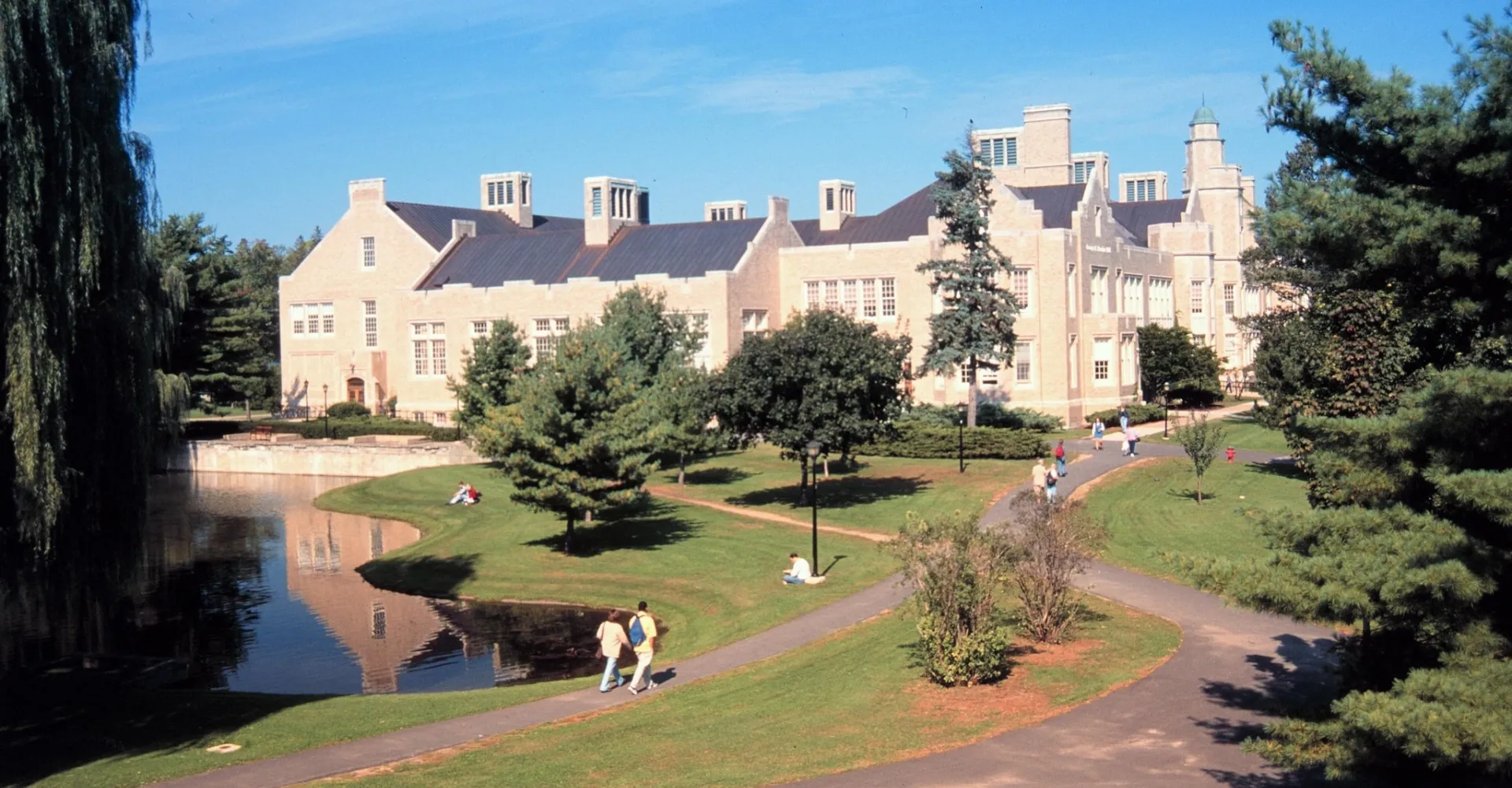 Il grande edificio della SUNY Plattsburgh accanto a un laghetto con aree verdi e viali nel campus.