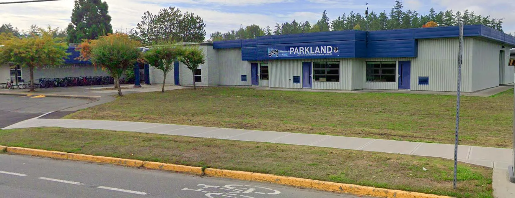 El moderno edificio azul de la Parkland Secondary School está rodeado por una zona verde y árboles.