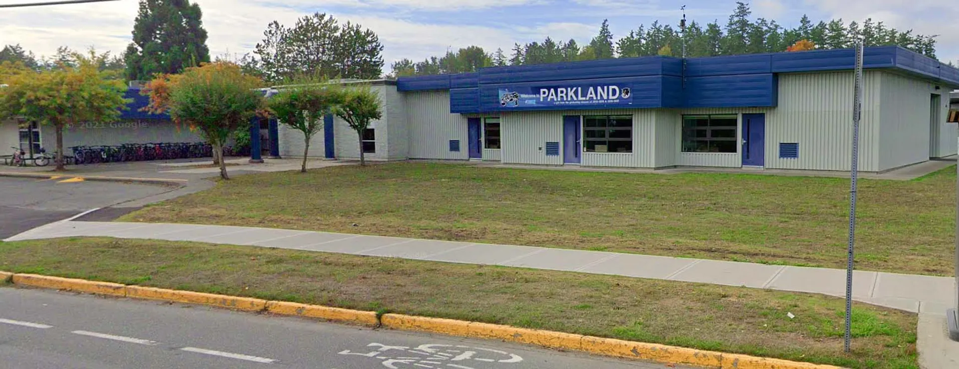 Il moderno edificio blu della Parkland Secondary School è circondato da un'area verde e da alberi.