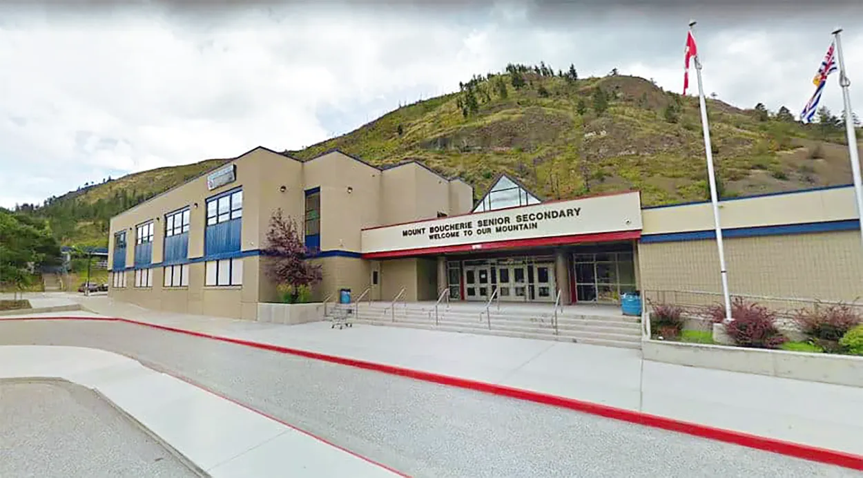 El moderno edificio escolar de la Mount Boucherie Secondary School con alfombra roja en la entrada frente a colinas verdes.