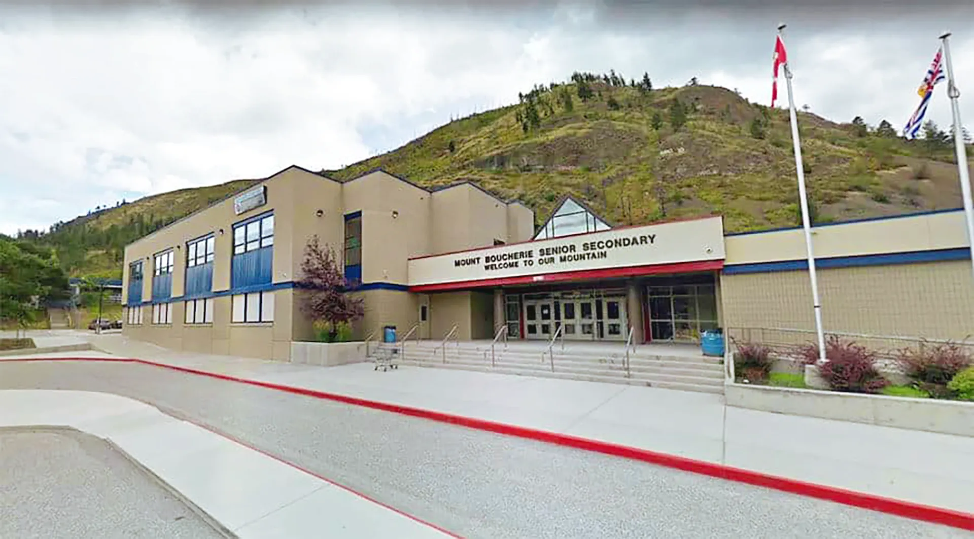 L'edificio scolastico moderno della Mount Boucherie Secondary School con un tappeto rosso all'ingresso davanti a verdi colline.