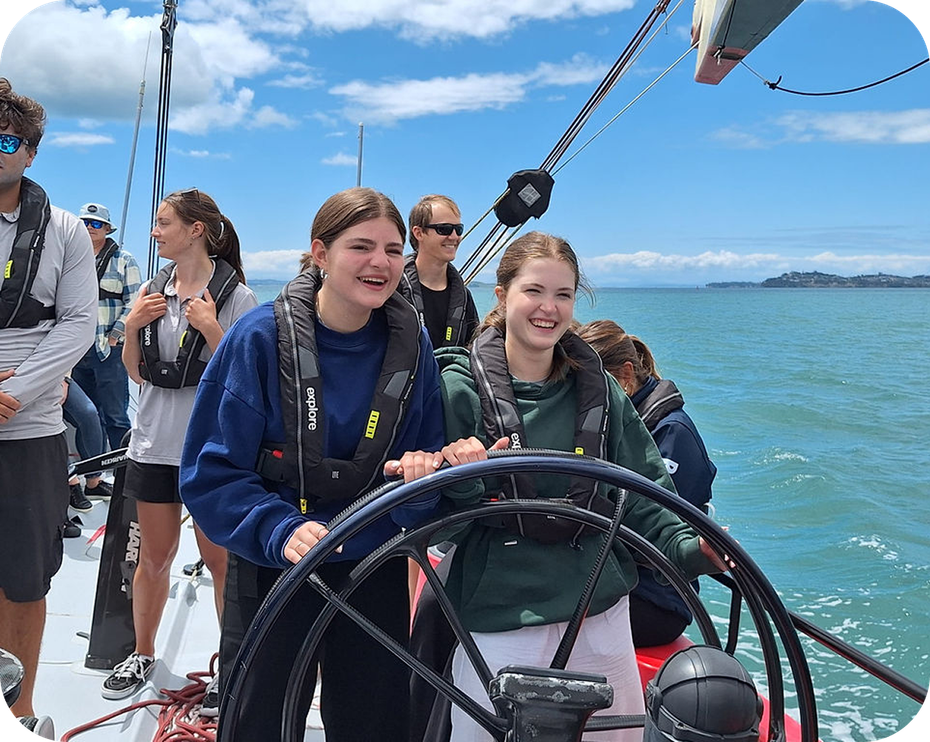 Dos estudiantes con chaleco salvavidas al timón de un velero en el mar