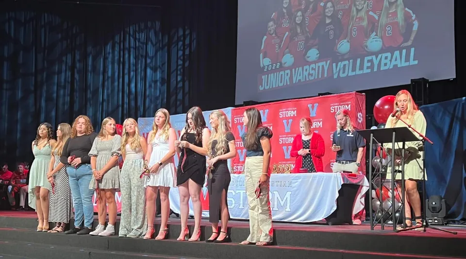Un gruppo di donne si trova sul palco durante un evento di Junior University Volleyball nel campus della Victory Christian Academy.