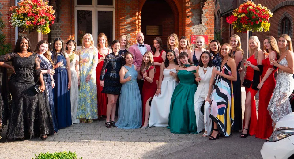 Un gruppo di persone vestite elegantemente sta davanti a un edificio in mattoni nel campus di St. George's Ascot.