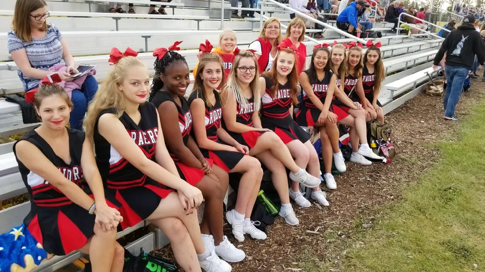 Un gruppo di giovani cheerleader in uniforme rossa e nera siede sulle tribune della Lindsay Thurber Comprehensive High School.