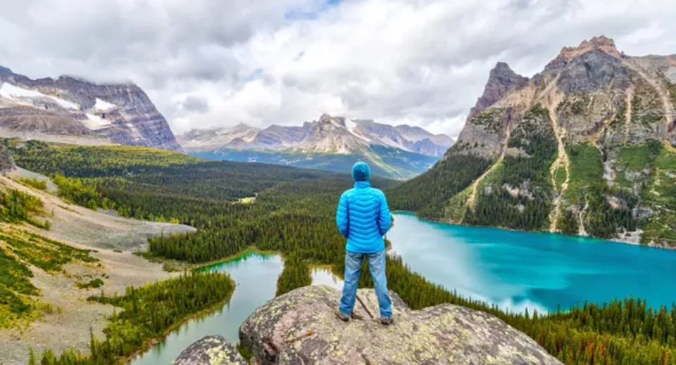 Una persona in abiti blu si trova su una roccia con vista sul paesaggio montano e sul lago vicino alla Abbotsford Senior Secondary School.