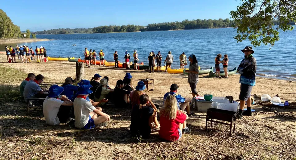 Un gruppo di studenti della Centenary Heights State High School si riunisce sulla riva del lago circondato da alberi.