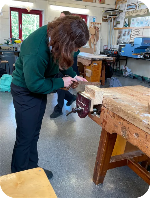 Estudiante con uniforme trabaja la madera con un tornillo de banco en el taller de tecnología
