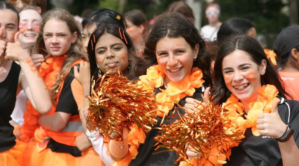Studenti della Hutt Valley High School vestiti di arancione e giallo mostrano i loro pompon durante un'esibizione di cheerleading all'aperto.