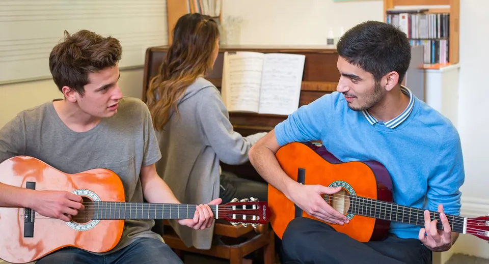 Tre studenti della MPW London suonano la chitarra in una stanza con scaffali di libri.