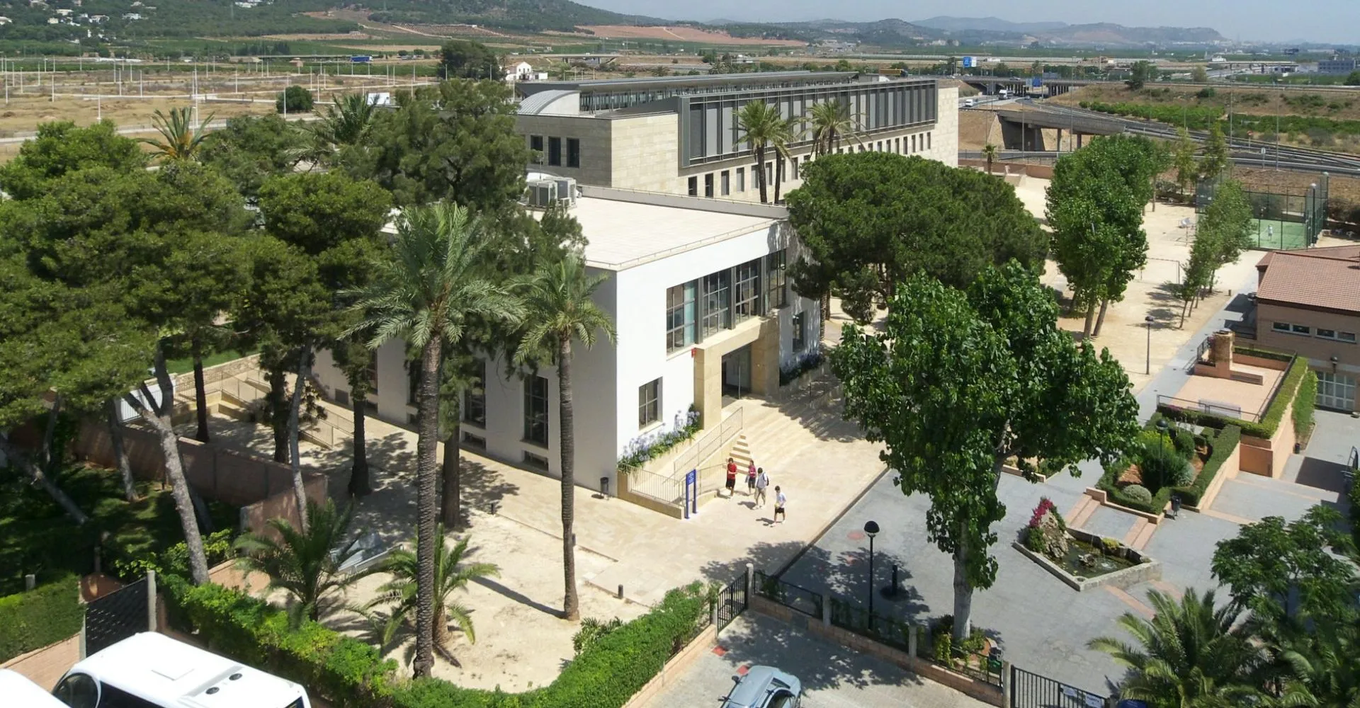 L'edificio moderno del Caxton College è circondato da palme e aree verdi con studenti che camminano sul vialetto pavimentato.