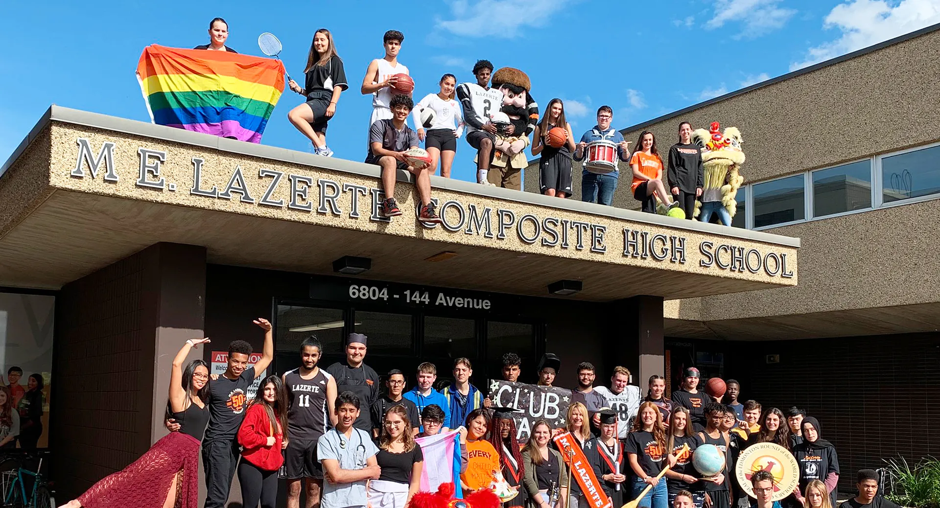 Studenti e membri dello staff della M.E. LaZerte Composite High School sono davanti all'edificio scolastico con una ben visibile bandiera arcobaleno.
