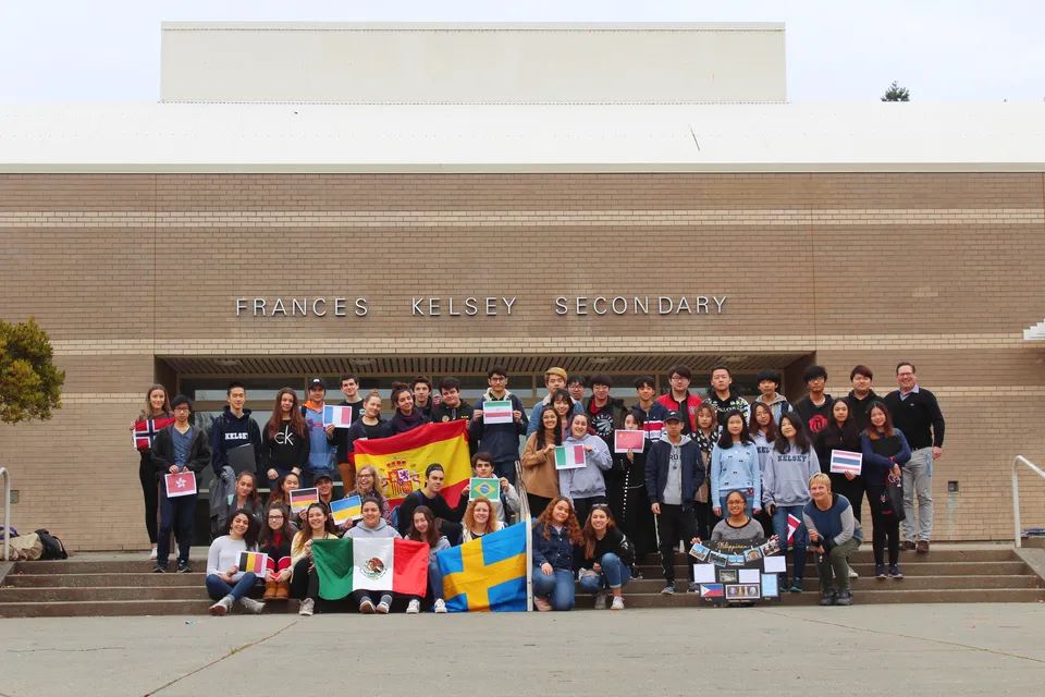 Un gruppo di giovani posa con bandiere nazionali davanti all'edificio della Frances Kelsey Secondary School.