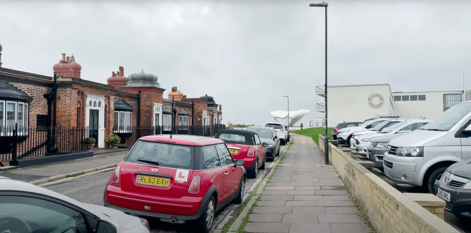 Straße in Bexhill-on-Sea mit roten Backsteinhäusern und parkenden Autos, am Ende der Straße die Küste