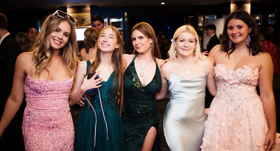 Cinque studentesse del Whangaparāoa College posano insieme durante un evento formale su sfondo scuro.
