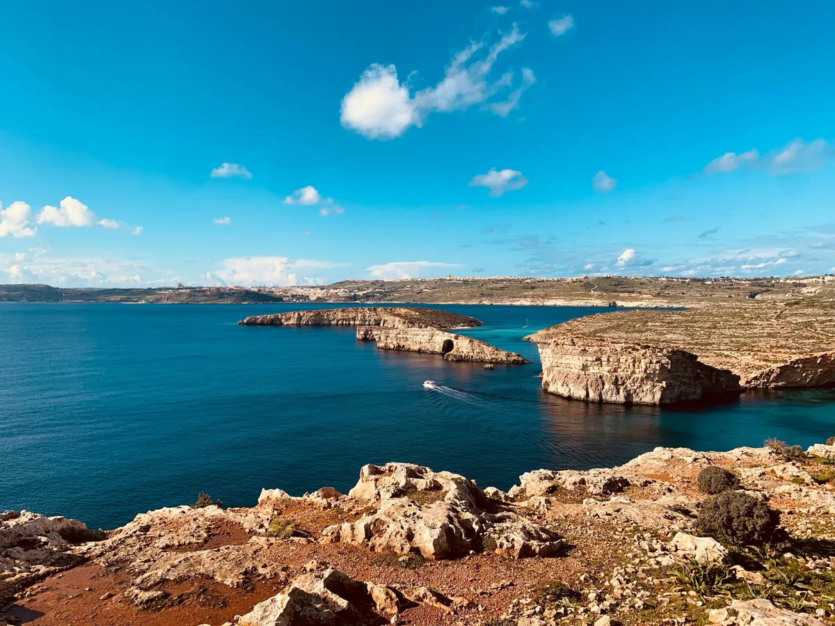 Costa rocciosa di Malta con mare turchese e una piccola barca all'imbocco della baia