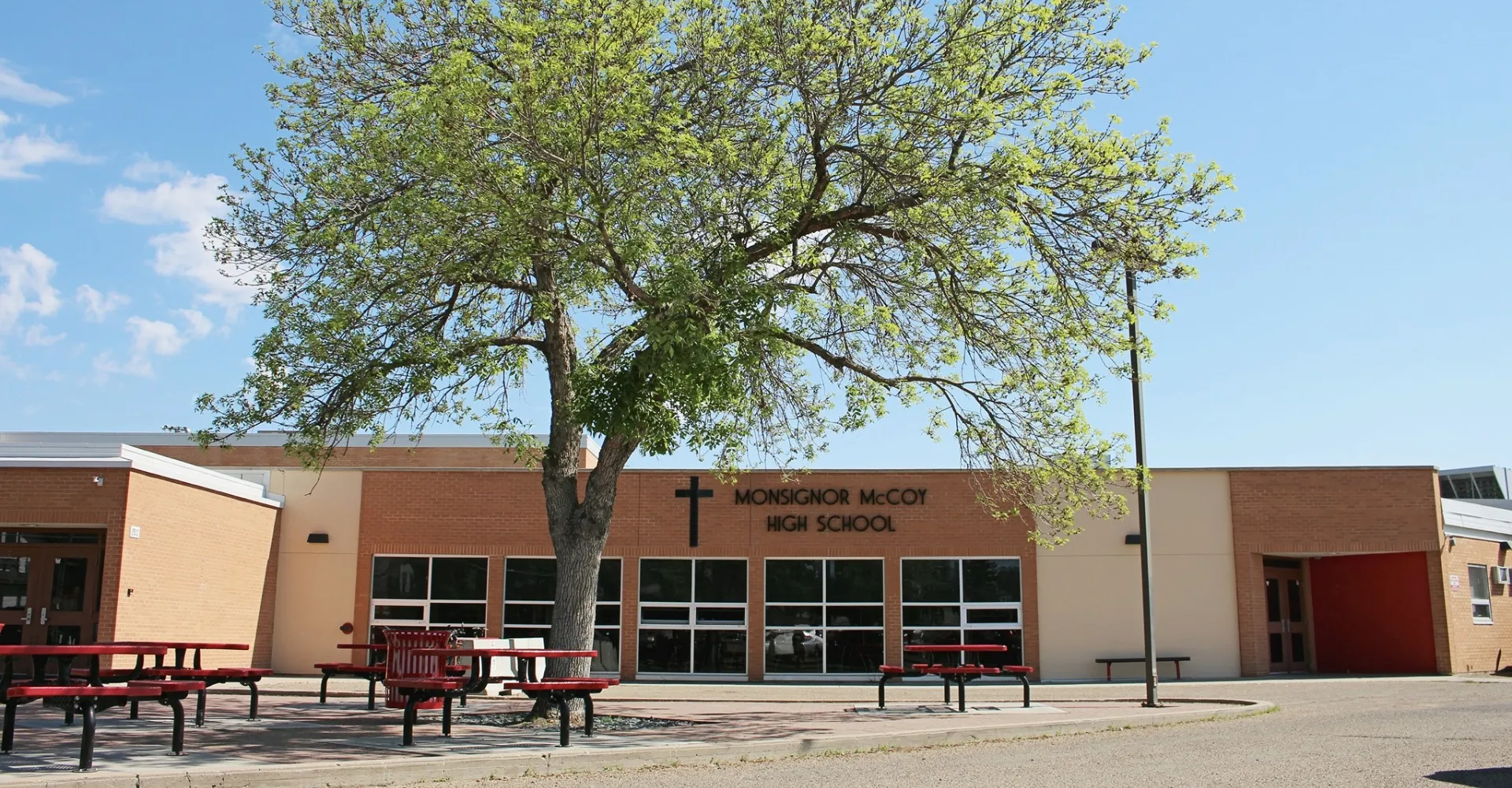 Un grande albero con un folto fogliame verde si trova davanti all'edificio in mattoni della Monsignor McCoy High School.