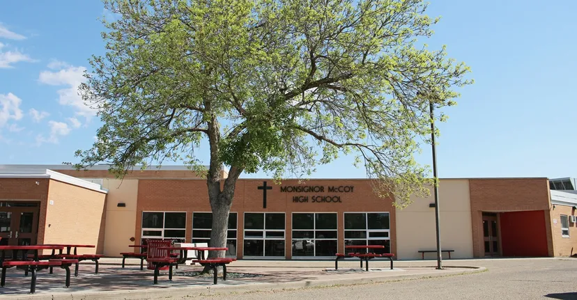 Un grande albero con un folto fogliame verde si trova davanti all'edificio in mattoni della Monsignor McCoy High School.