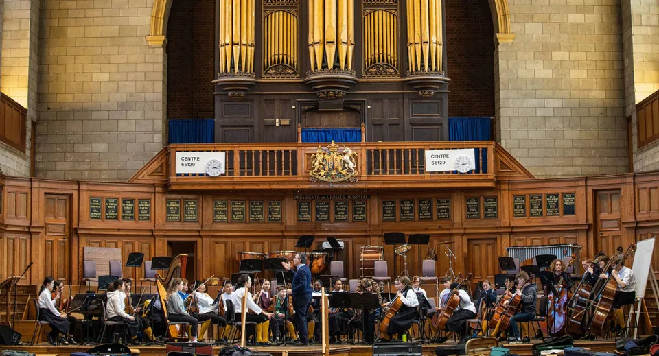 L'orchestra scolastica della Christ's Hospital School prova con un direttore davanti a un grande organo a canne.