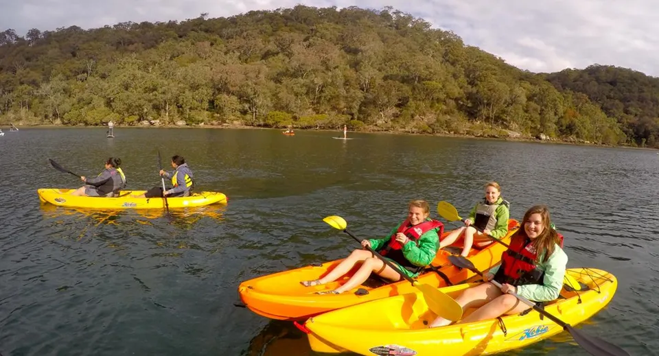 Studenti del Coláiste an Chreagáin pagaiano in kayak gialli su un lago davanti a colline boscose.