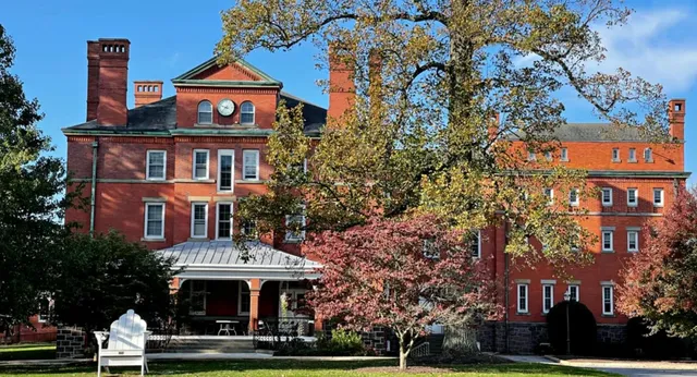 Il storico edificio in mattoni della Westtown School con una torre si trova circondato da alberi colorati d'autunno sotto un cielo blu terso.