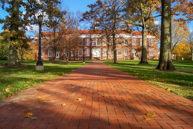 Un viale pavimentato attraversa il campus alberato della Western Reserve Academy, con un edificio in mattoni e i colori dell'autunno sullo sfondo.
